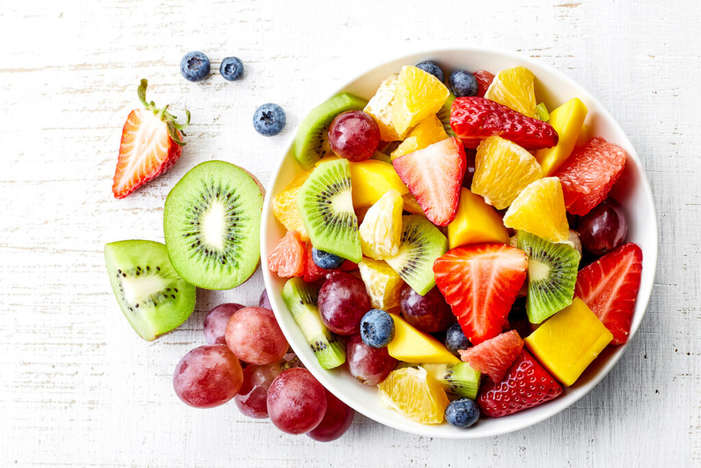 Top view of a bowl of healthy fresh fruit salad on wooden background