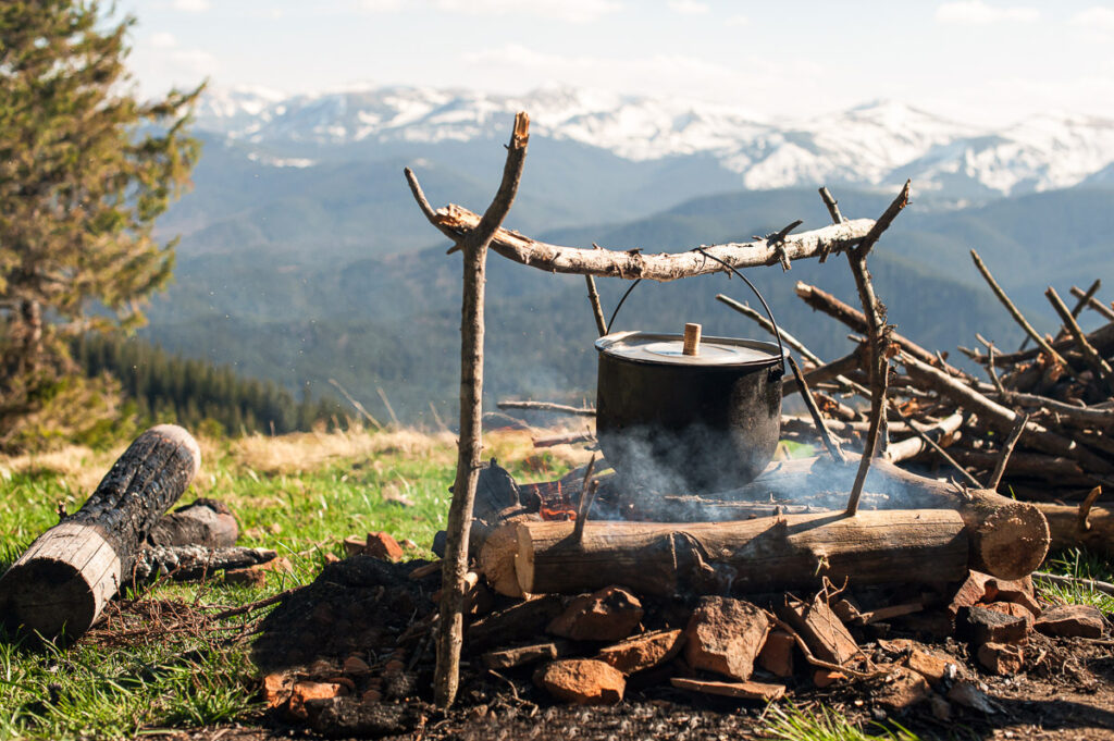An old little boiler is heated on a fire on a green mountain meadow among the mountains