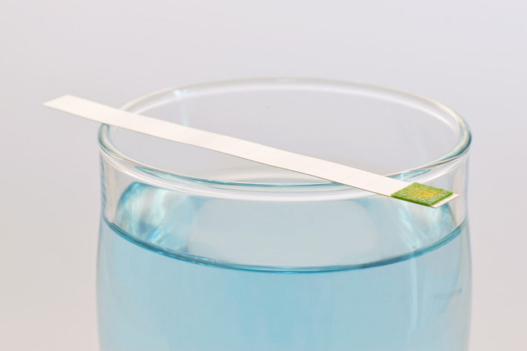 a glass with blue water and a testing stick that is indicating hard water