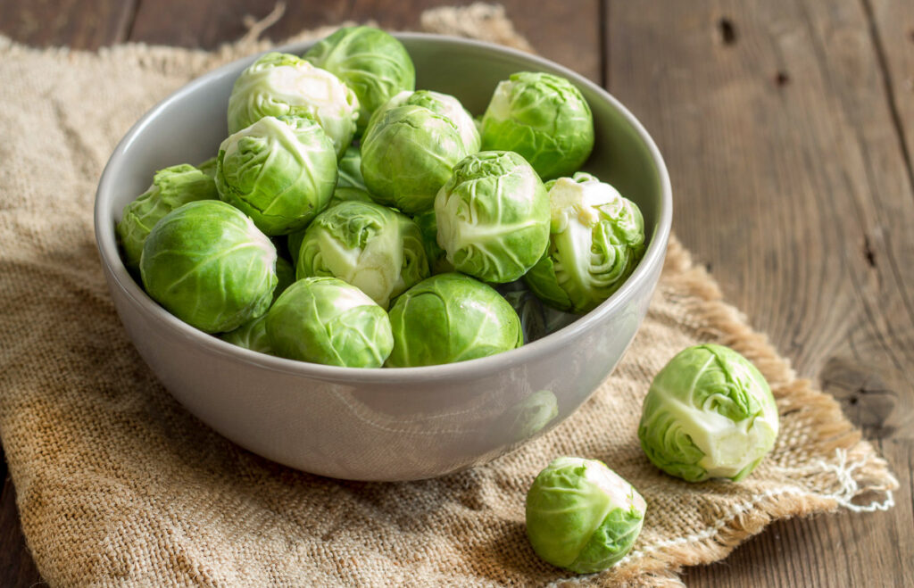 Brussels sprouts in a bowl and a few on burlap on an old wooden table
