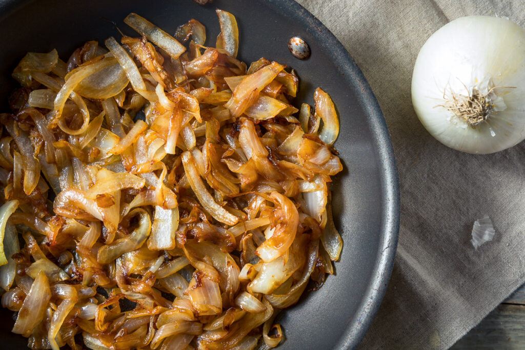 A non-stick pan with caramelized onions in it with an onion on a napkin