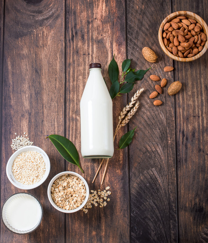 Plant based milk, healthy alternative drink in bottle on wooden background, ingredients for plant milk, almond, oat, rice milk, flat lay