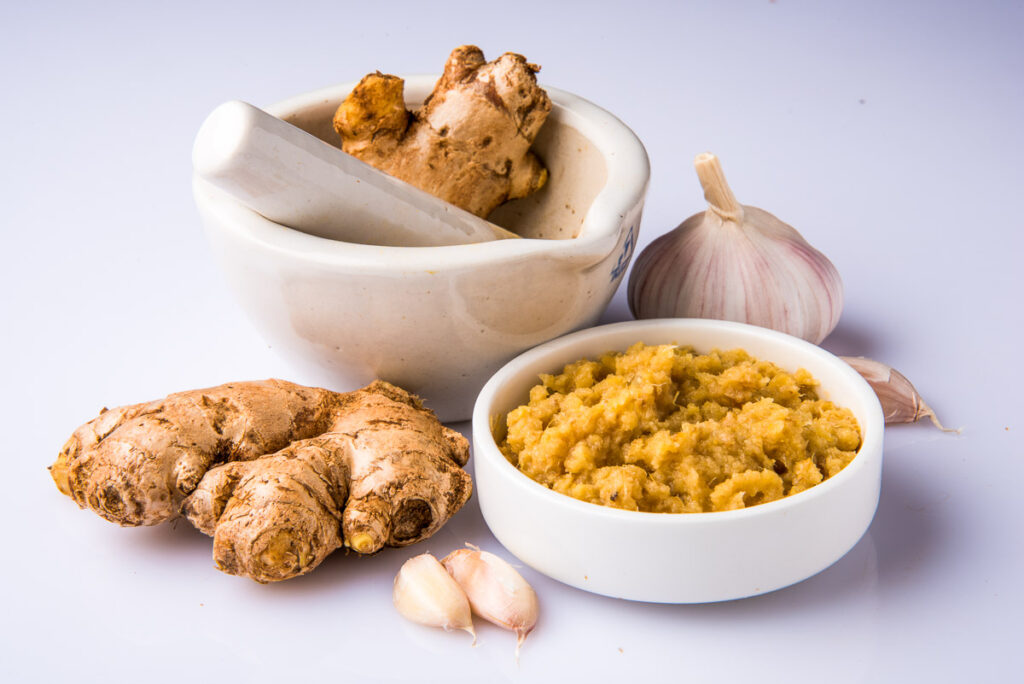 A white table with ginger and garlic on it along with a small white bowl and mortar and pestle