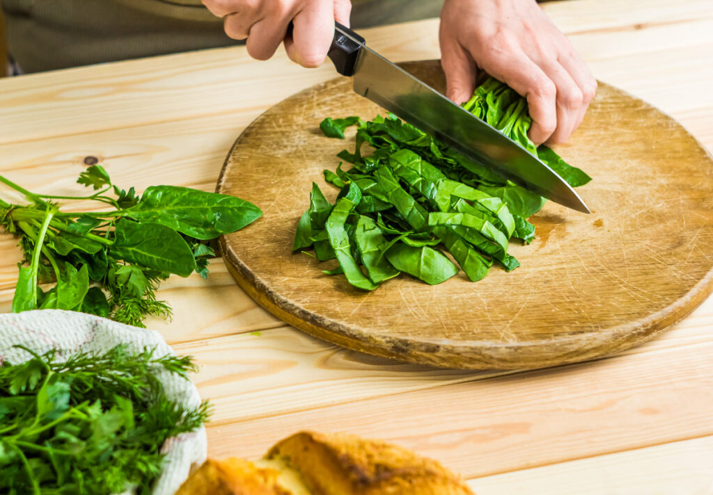 A woman's hands chopping spinach on a round wooden board