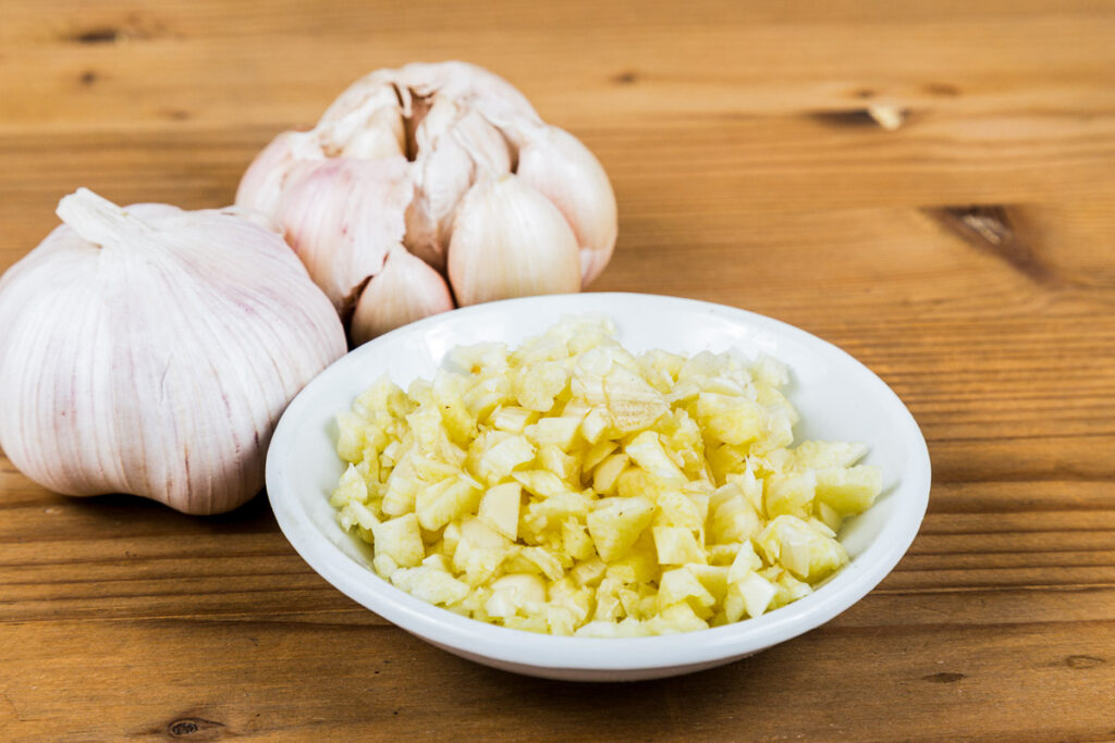 chopped garlic in white bowl with bulbs in the back