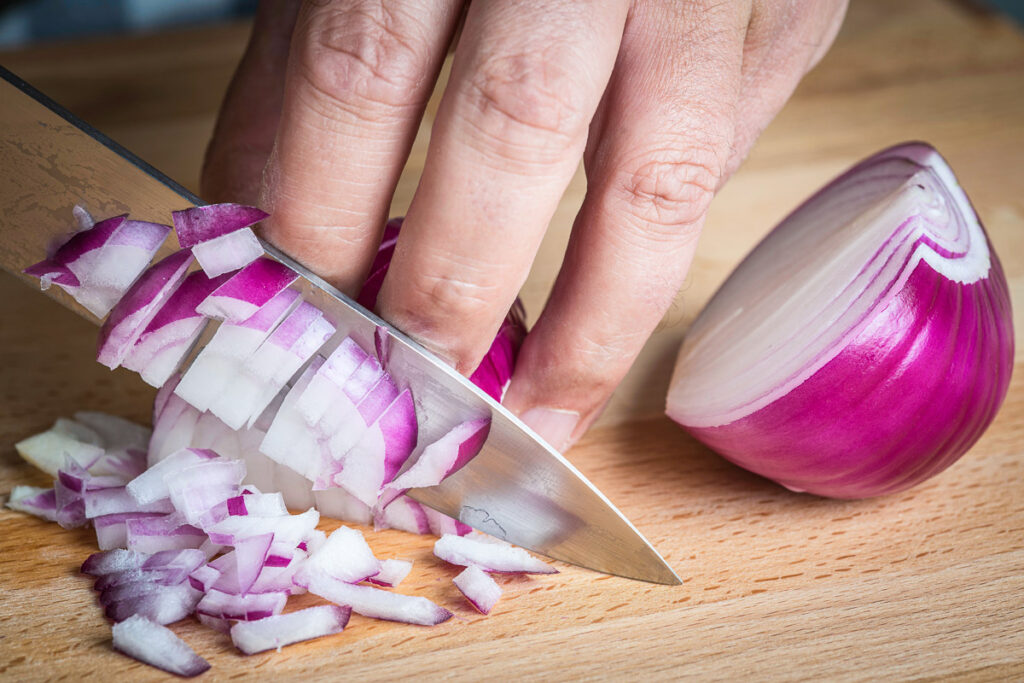 Chef choppig a red onion with a knife on the cutting board
