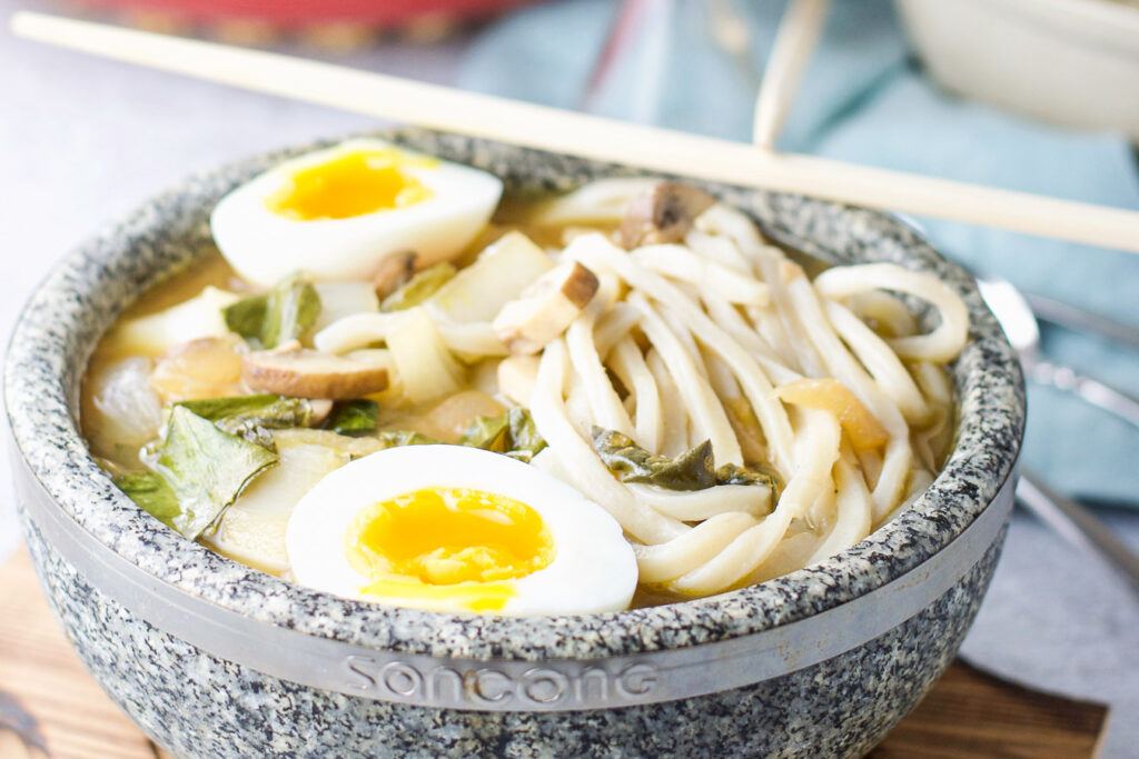A stone bowl filled with umami soup with noodles and soft boiled eggs