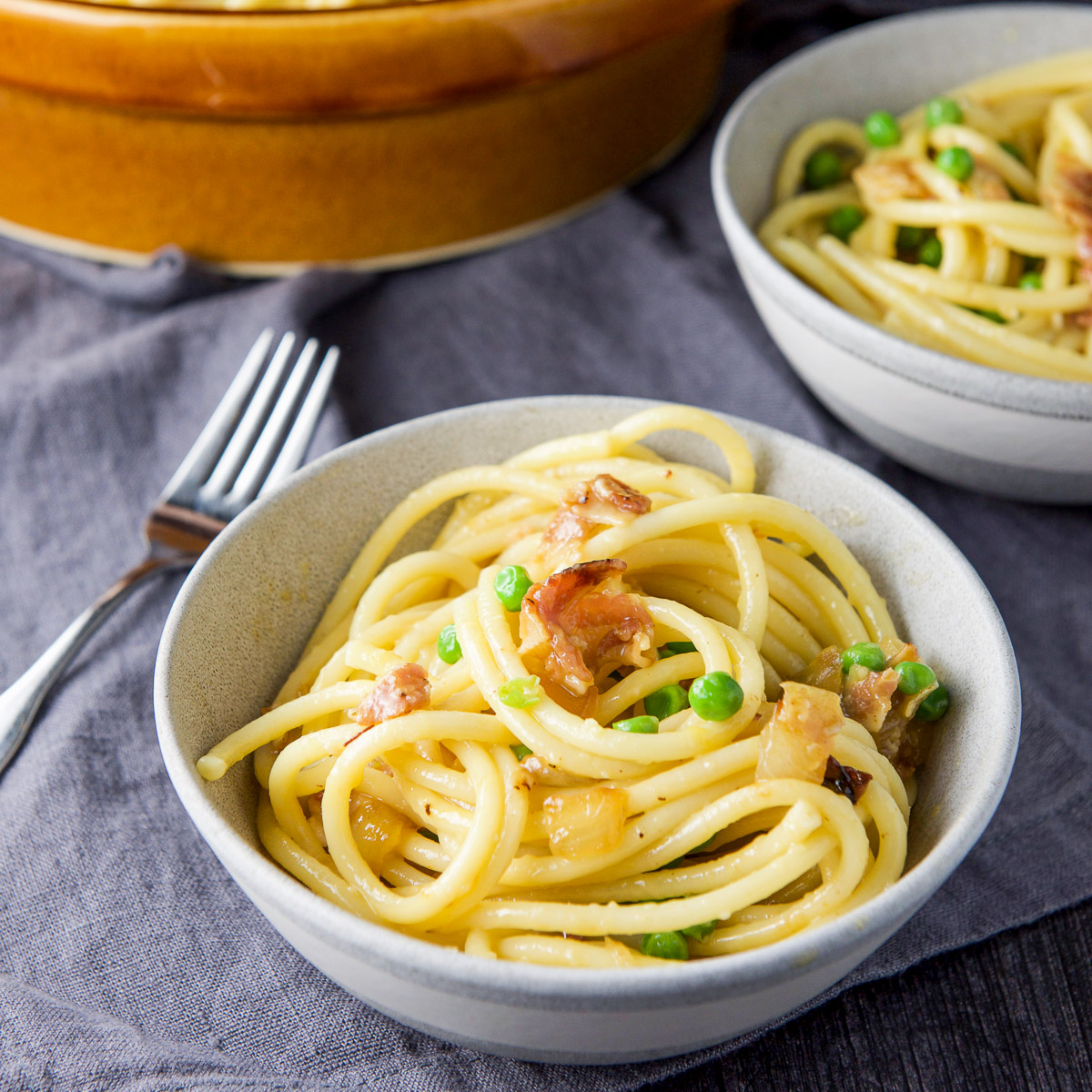 Two grey bowls filled with carbonara with peas and pancetta