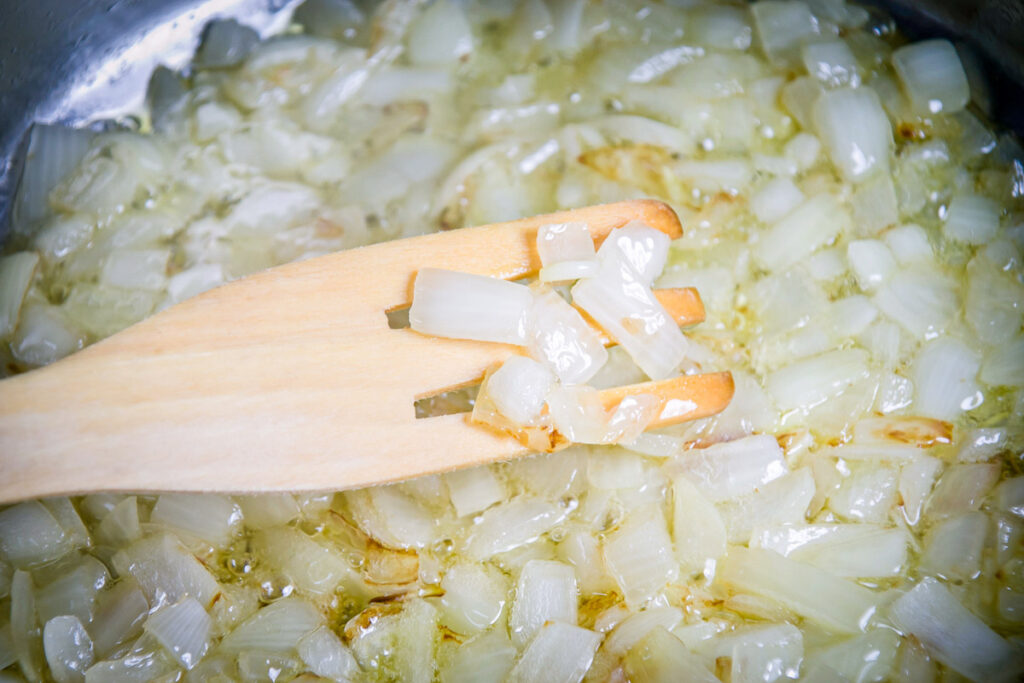 A wooden fork holding onion pieces over a pan sauteing the vegetable