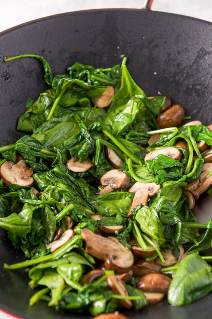 A wok filled with sautéed spinach and mushrooms
