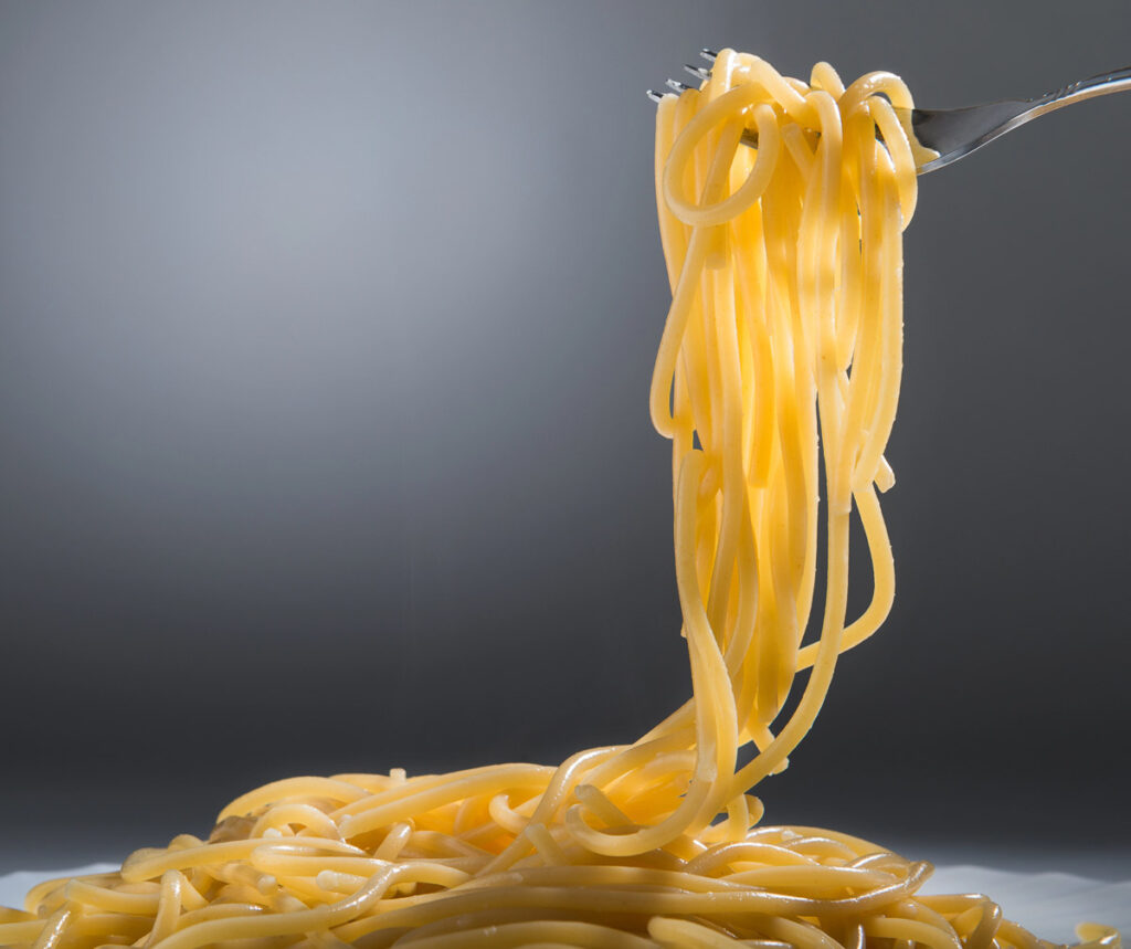 A fork with al dente spaghetti on it being held in the air over a pile of pasta