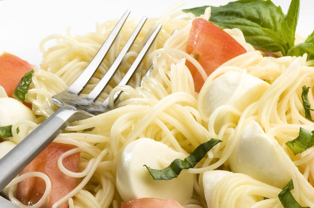 a fork on a pile of spaghettini, tomatoes, basil, and mozzarella pearls