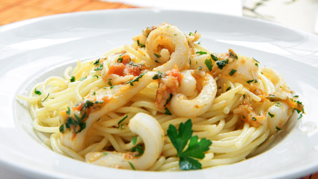 a white plate with seafood on pasta with tomato and parsley